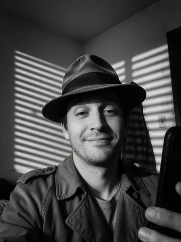 Exempel på Film noir: Bilden blir en svartvit film noir-scen från 1940-talet, där personen bär trenchcoat och hatt och persiennskuggor faller på väggen.