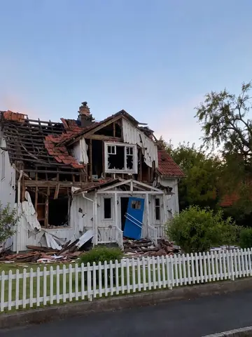 Exempel på Huset i spillror: Huset bakom personen ser ut att just ha rasat ihop, utan fordon, logotyper eller text.