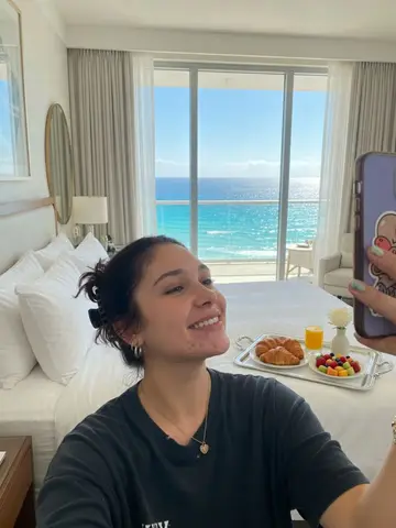 Exempel på Rumsservice: Personen befinner sig i en svit på ett femstjärnigt hotell med vita lakan, en silverbricka med frukt och croissanter och havsutsikt genom balkongdörrarna.