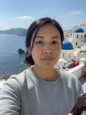 Exempel på Santorini: Personen sitter på en terrass på Santorini med vita hus, blå kupoler och det glittrande Egeiska havet bakom sig.